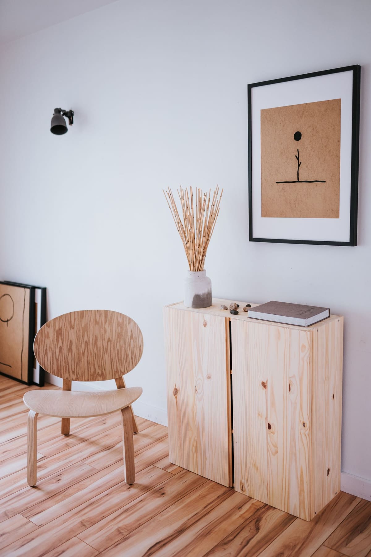 A wooden chair beside a timber cabinet with a framed print